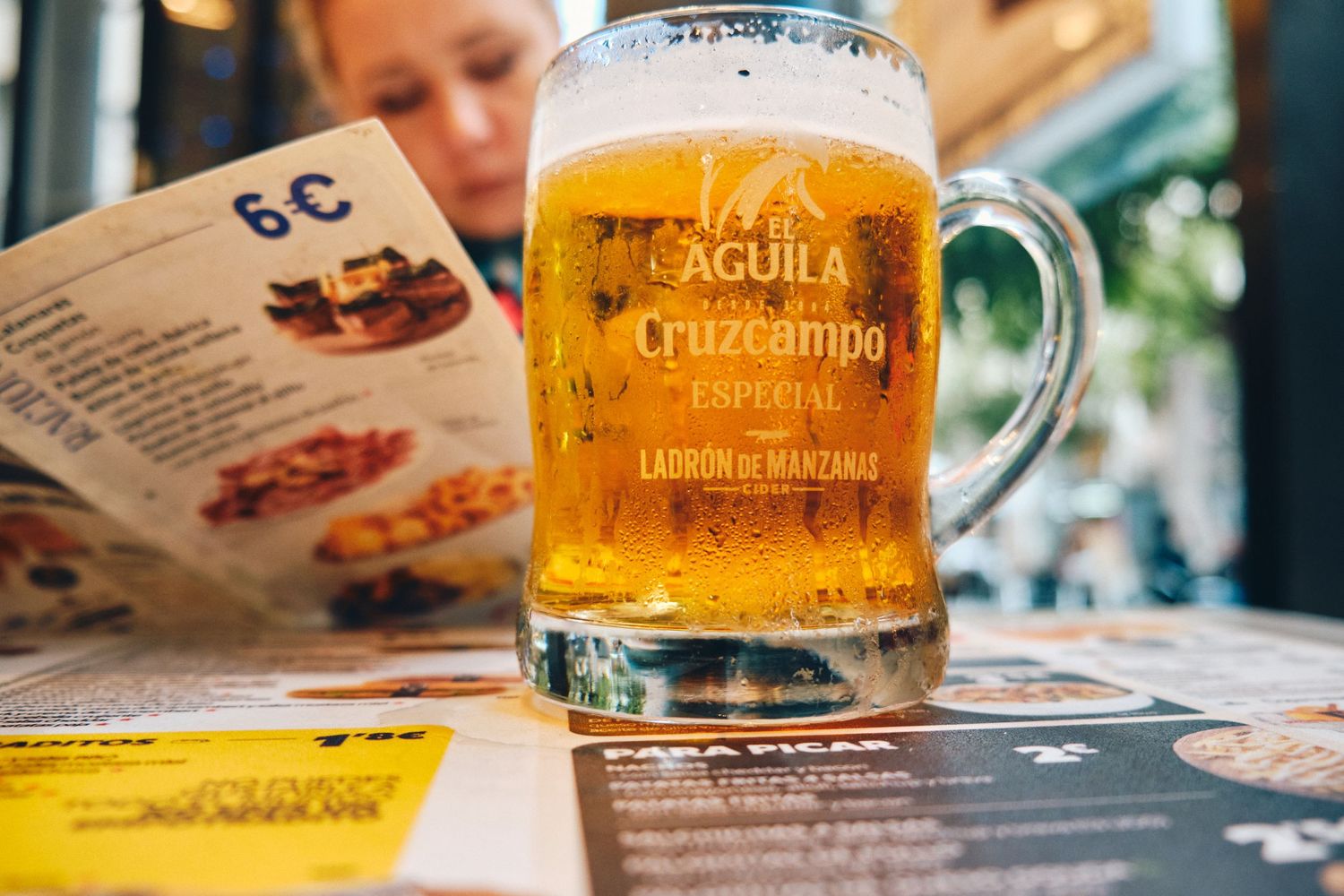 Glass of Aguila Cruzcampo beer sits on a menu at a restaurant.