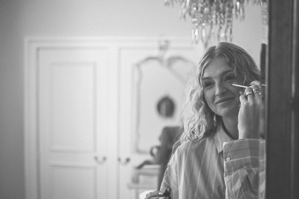 Black and white photo of person laughing while on phone in a room with elegant chandelier.