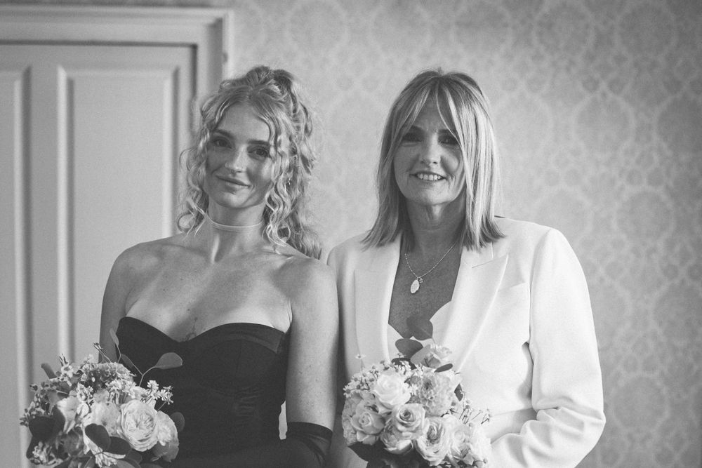 Two attendants in black and white attire hold bouquets at a wedding.