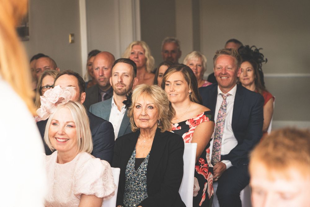 Wedding guests seated and smiling during indoor ceremony.