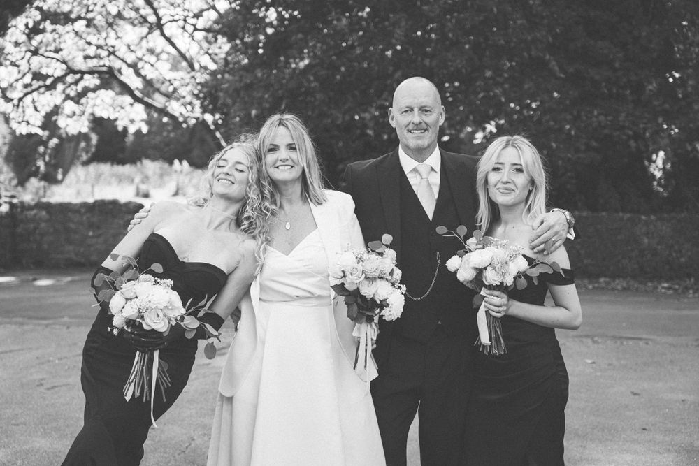 Elegant bridal party poses together for formal outdoor wedding photographs against a natural backdrop.