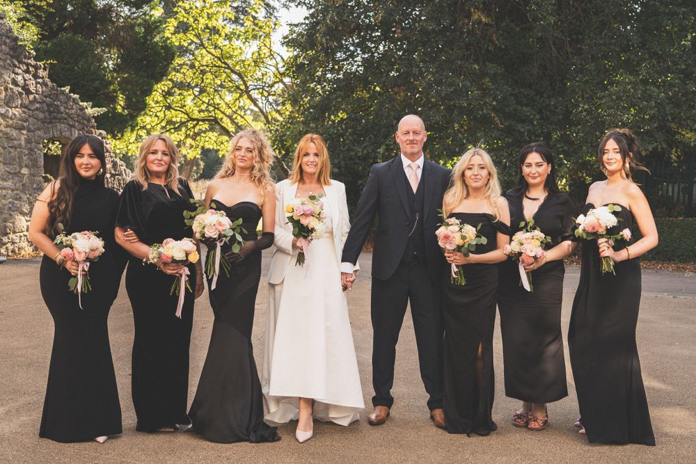 Wedding party wearing black and white attire poses in an outdoor garden setting.