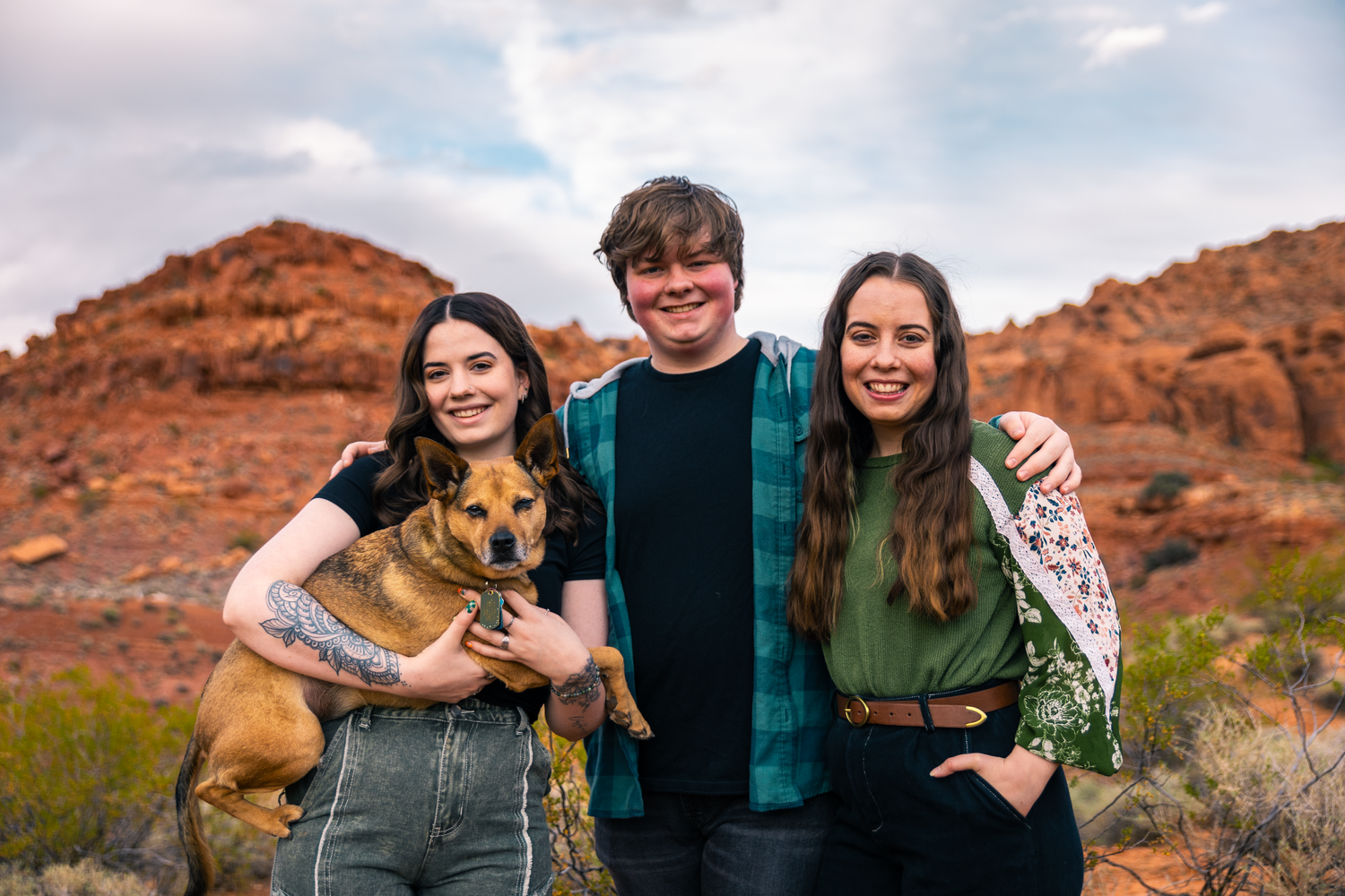 Three siblings and one holding a dog, with red rocks as the background