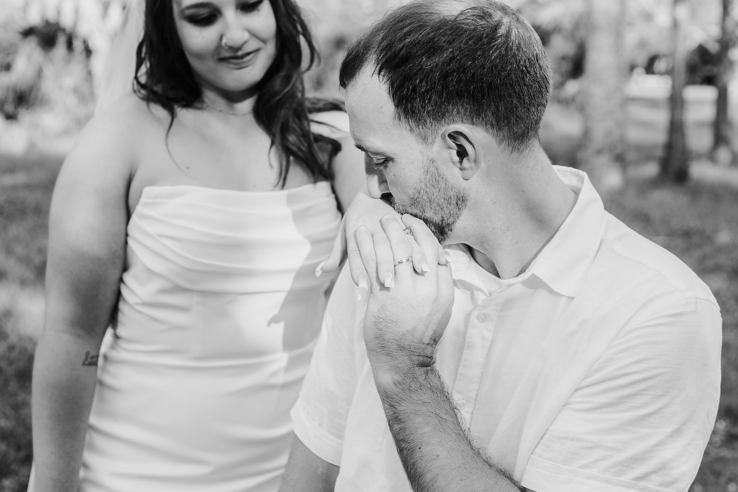 A tender black and white wedding moment captured outdoors showing an intimate gesture between the couple.