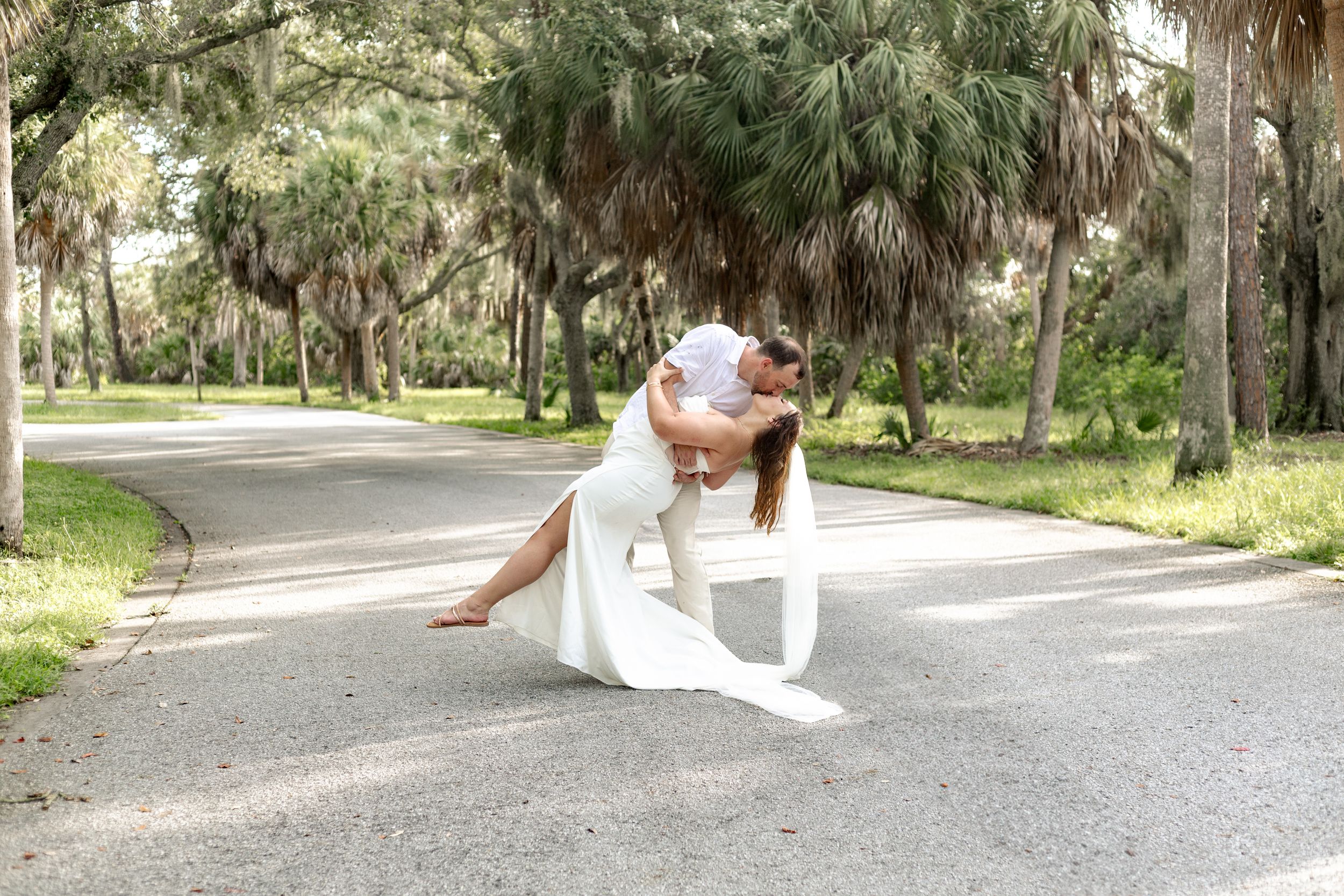 A playful wedding photo showing a couple dancing on a scenic palm-lined road.