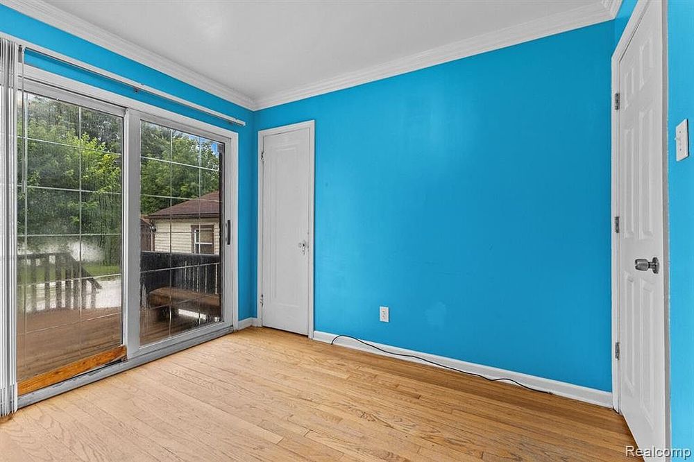 Empty room with bright blue accent walls, hardwood floors, and sliding glass door leading to outdoor deck.