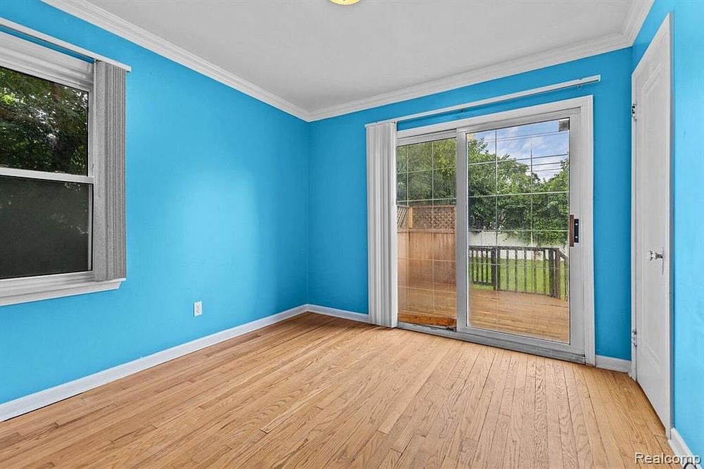 Bright blue room with hardwood floors, crown molding, and sliding glass door leading to outdoor deck.