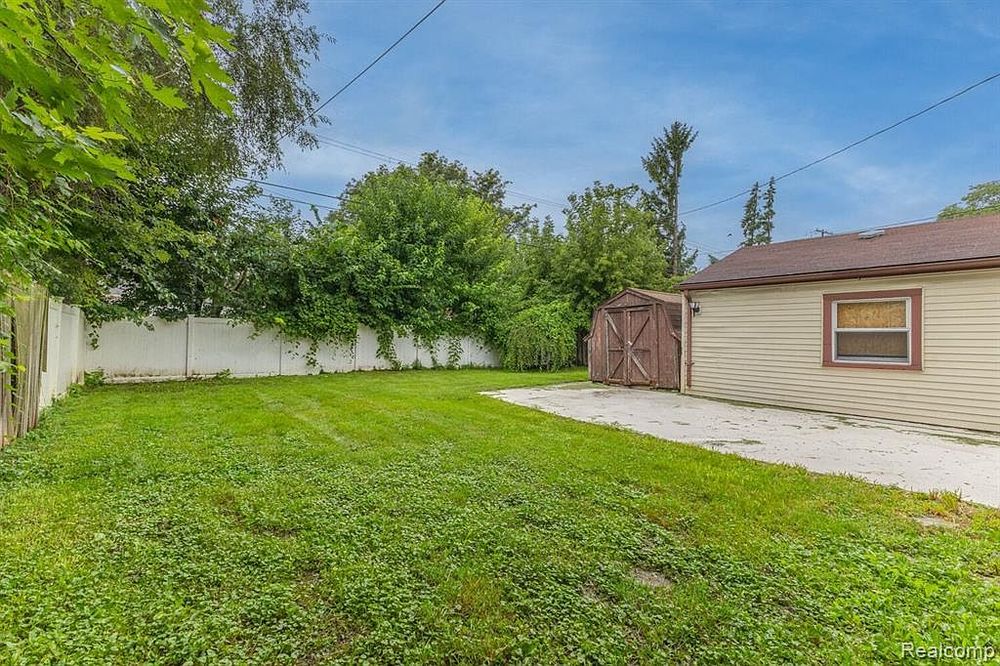 Spacious backyard with lush green lawn, privacy fence, mature trees, and detached storage shed.