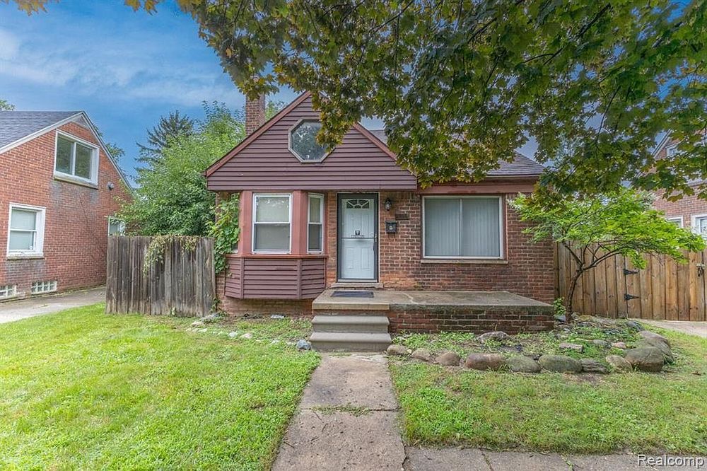 Charming red brick bungalow with manicured lawn and mature shade trees.