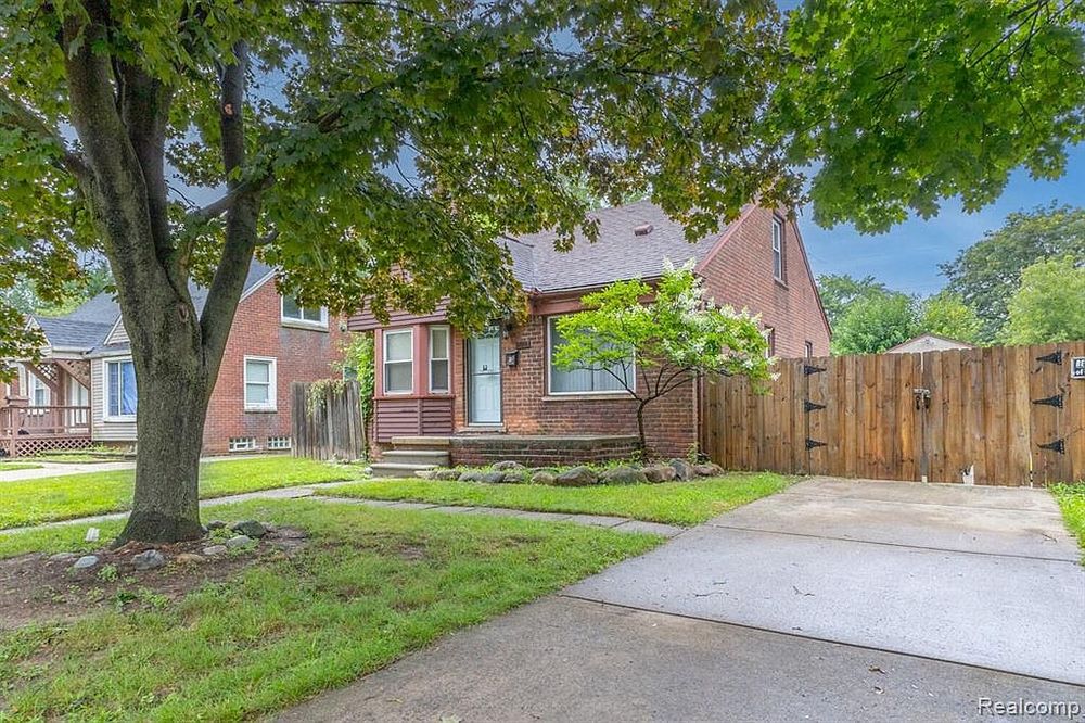Classic brick bungalow with large shade tree and concrete driveway.