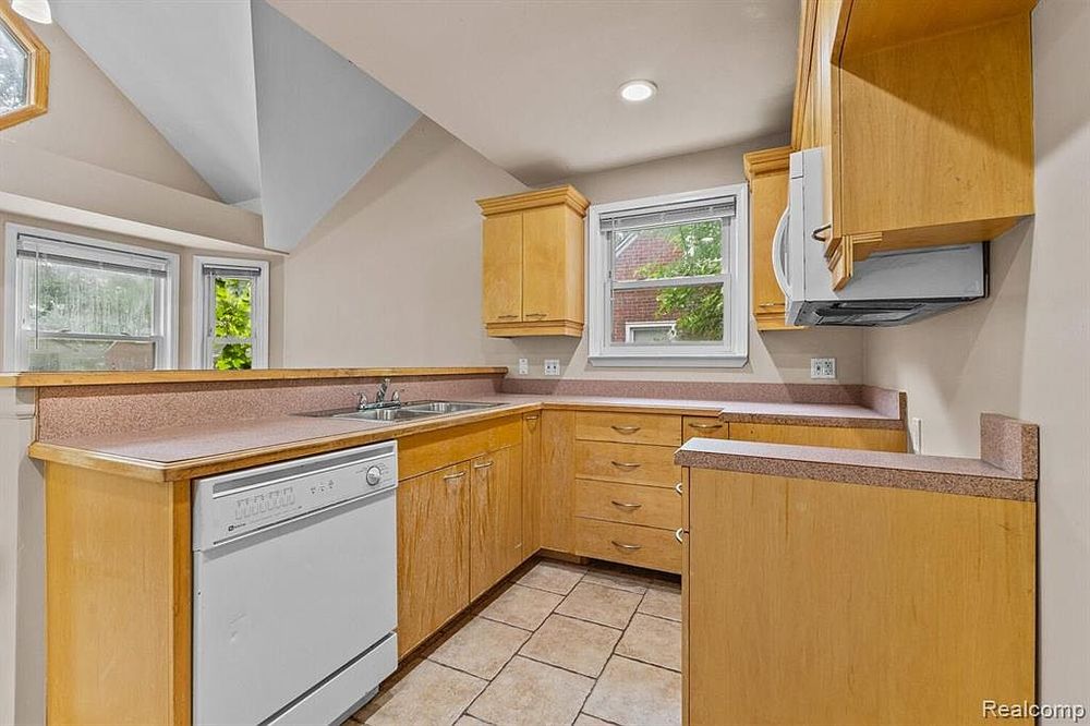 Bright kitchen with light wood cabinets, tile floors, and white dishwasher.