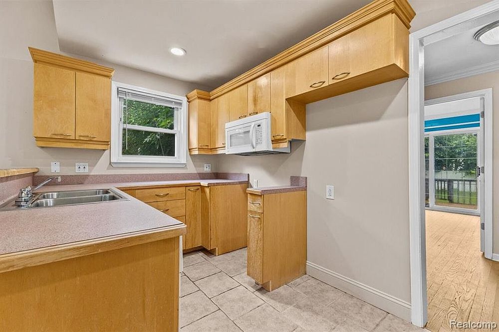 Kitchen with light maple cabinets, white appliances, single basin sink, and tile flooring with natural light.