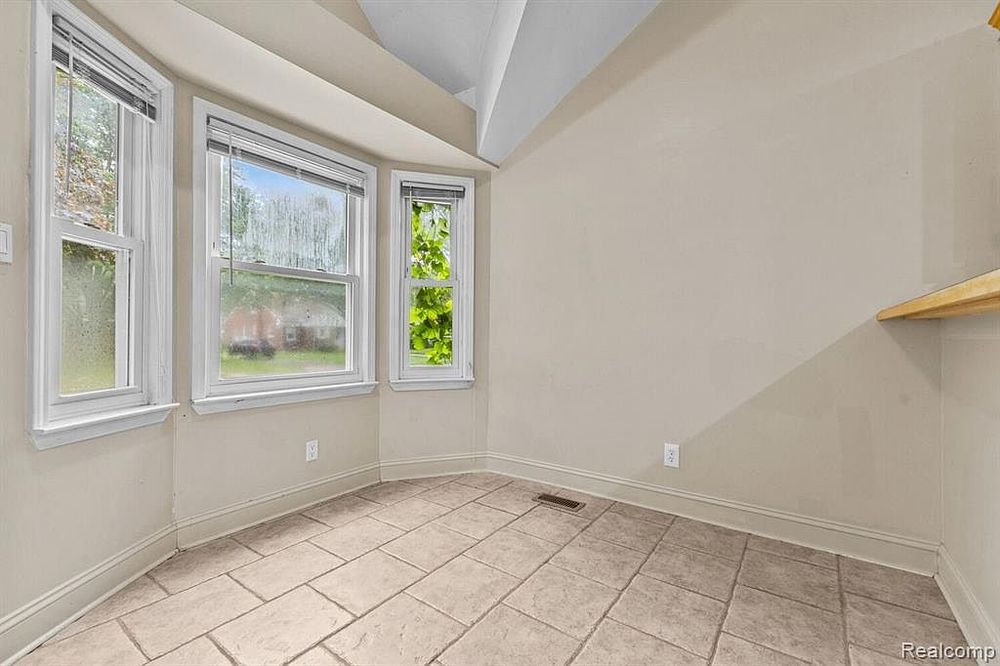 Bright breakfast nook with bay windows, tile flooring, vaulted ceiling, and a wooden shelf.