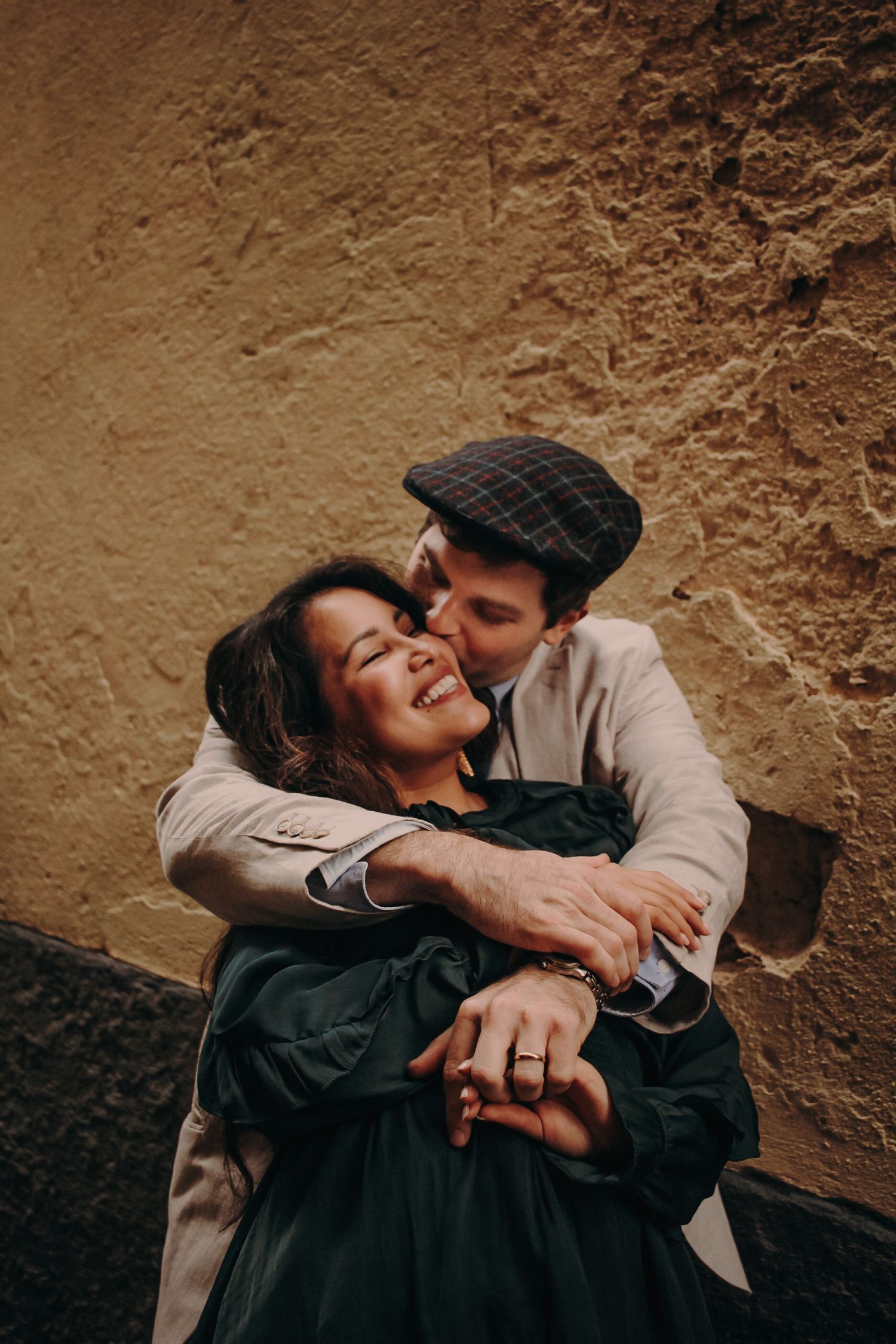 Intimate couple sharing a tender embrace against a textured brown wall.