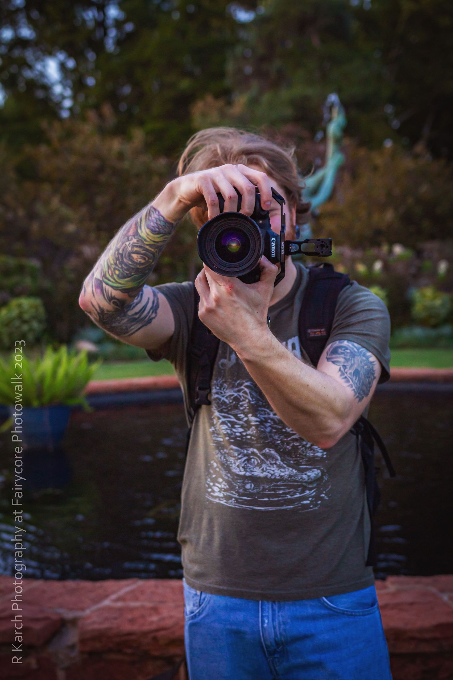 Tattooed photographer with camera taking photos in an outdoor garden setting.