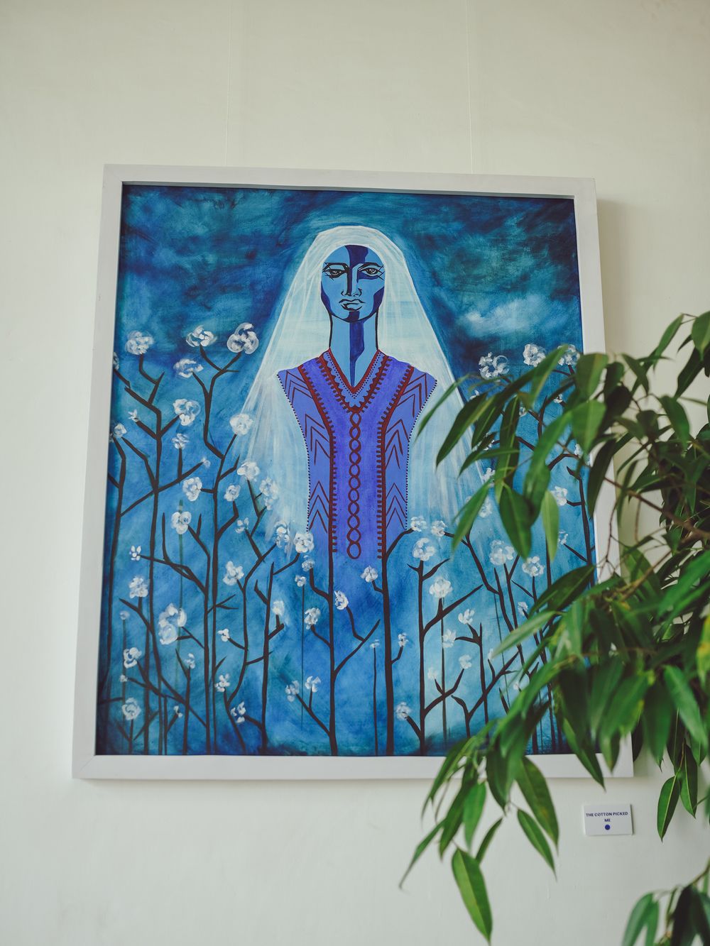Artistic portrait in blue tones depicting a figure among white floral elements against a dark background.