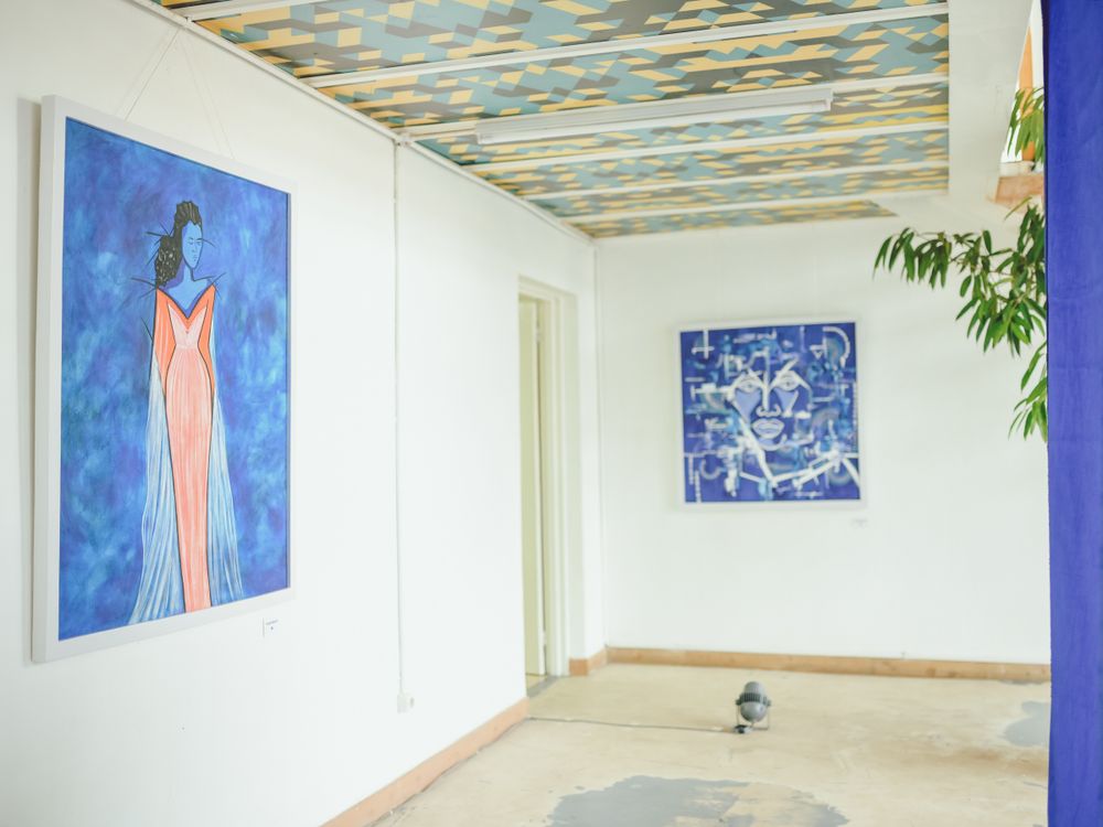 Art gallery interior with blue paintings and geometric patterned ceiling.