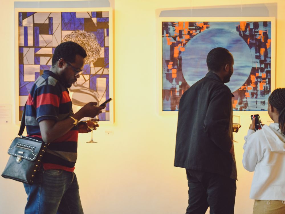 Gallery visitors viewing artwork displayed on warm yellow walls.