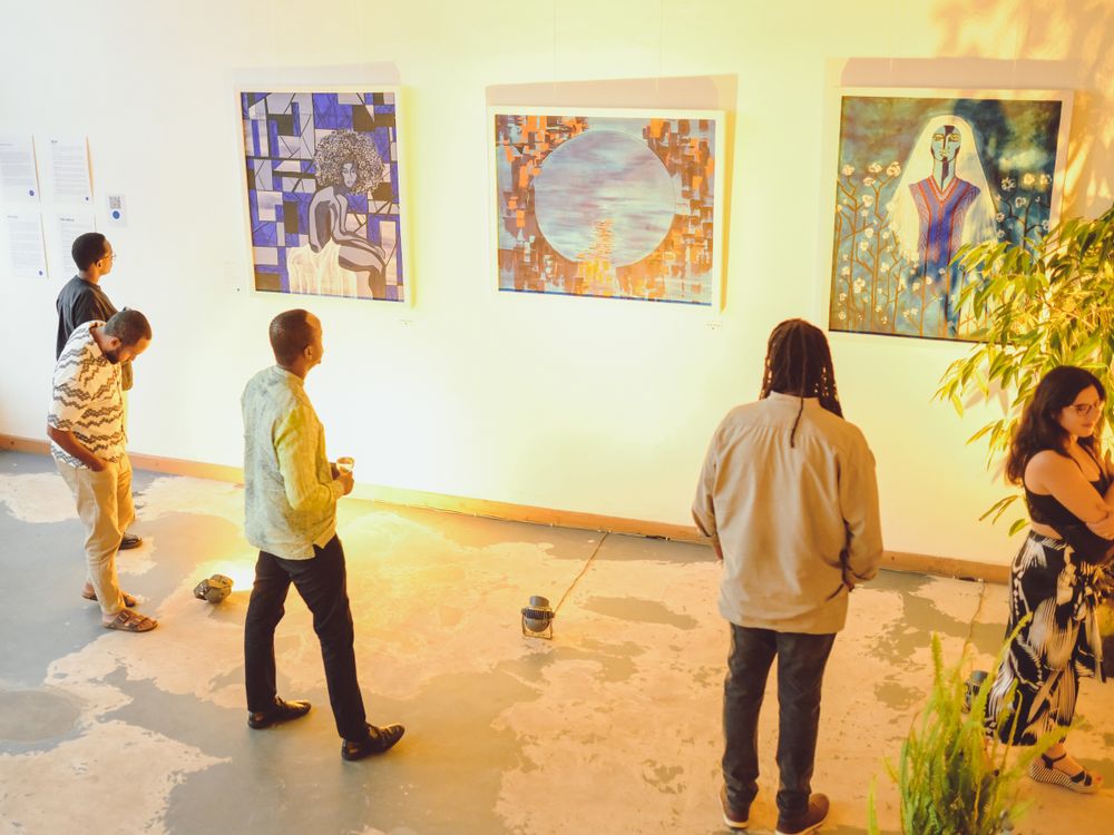 Art gallery visitors examining paintings on white walls with natural lighting.