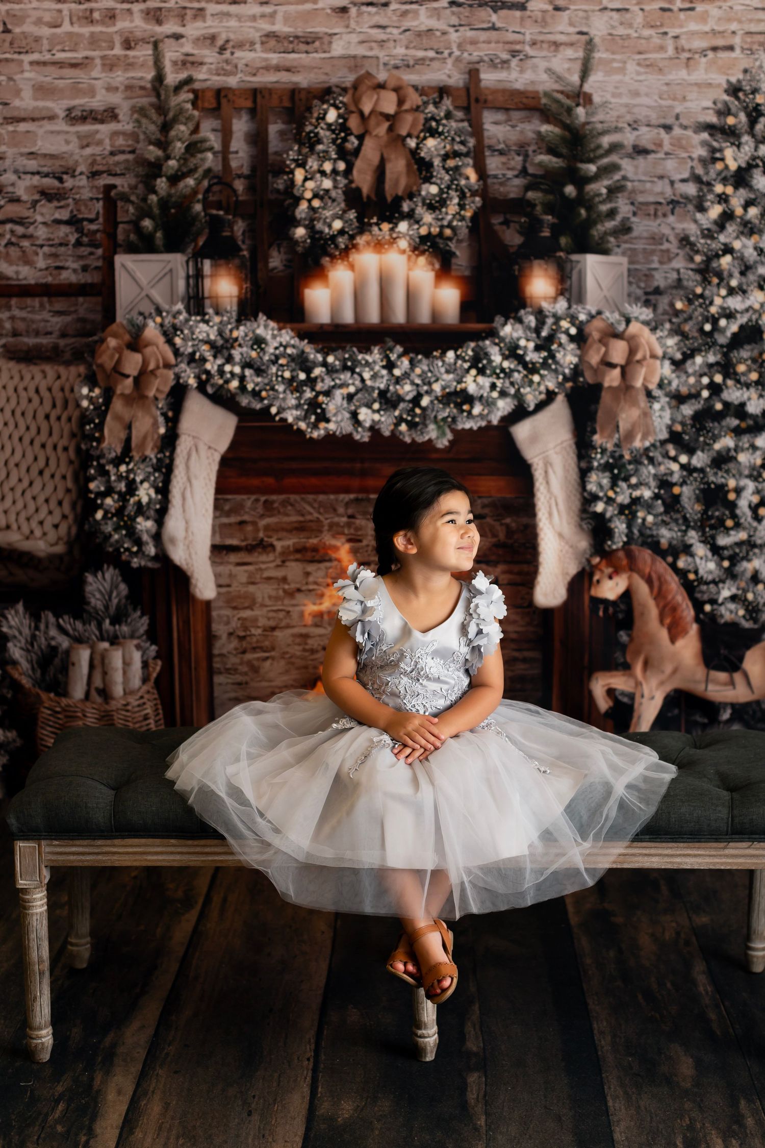 Child in white tulle dress poses on bench against Christmas decorated brick wall.