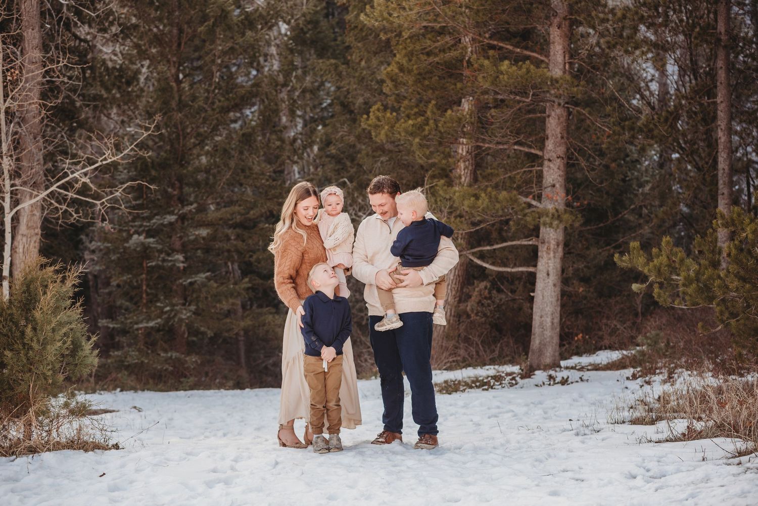 Four friends laughing and leaning together in a playful pose against a snowy winter backdrop.