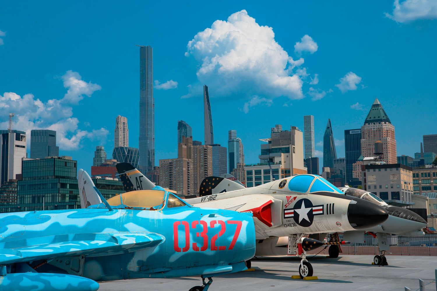 A blue and white military aircraft displayed on a rooftop with Manhattan skyline in background.