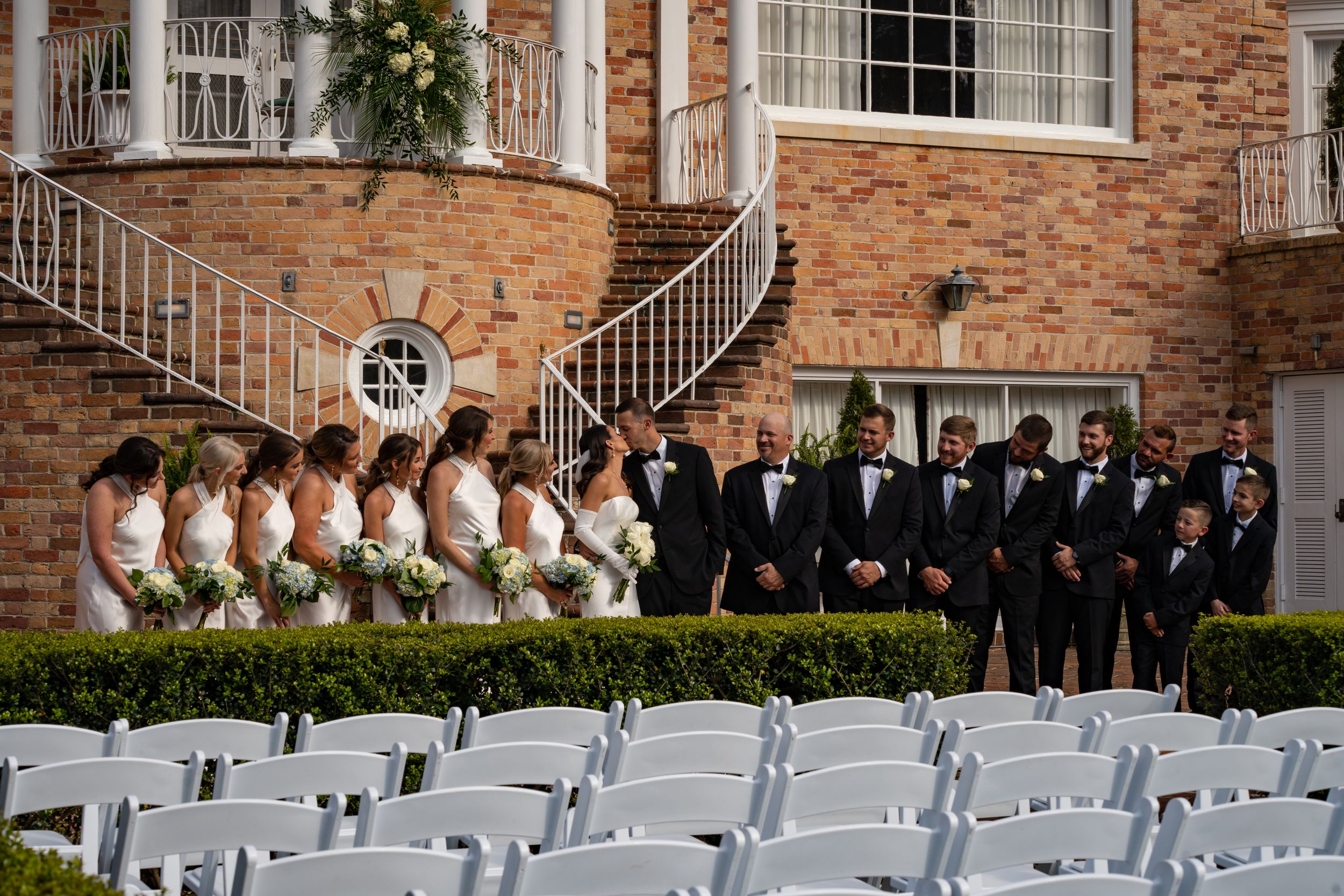 White chairs arranged in rows for an outdoor wedding ceremony at a historic brick building venue.