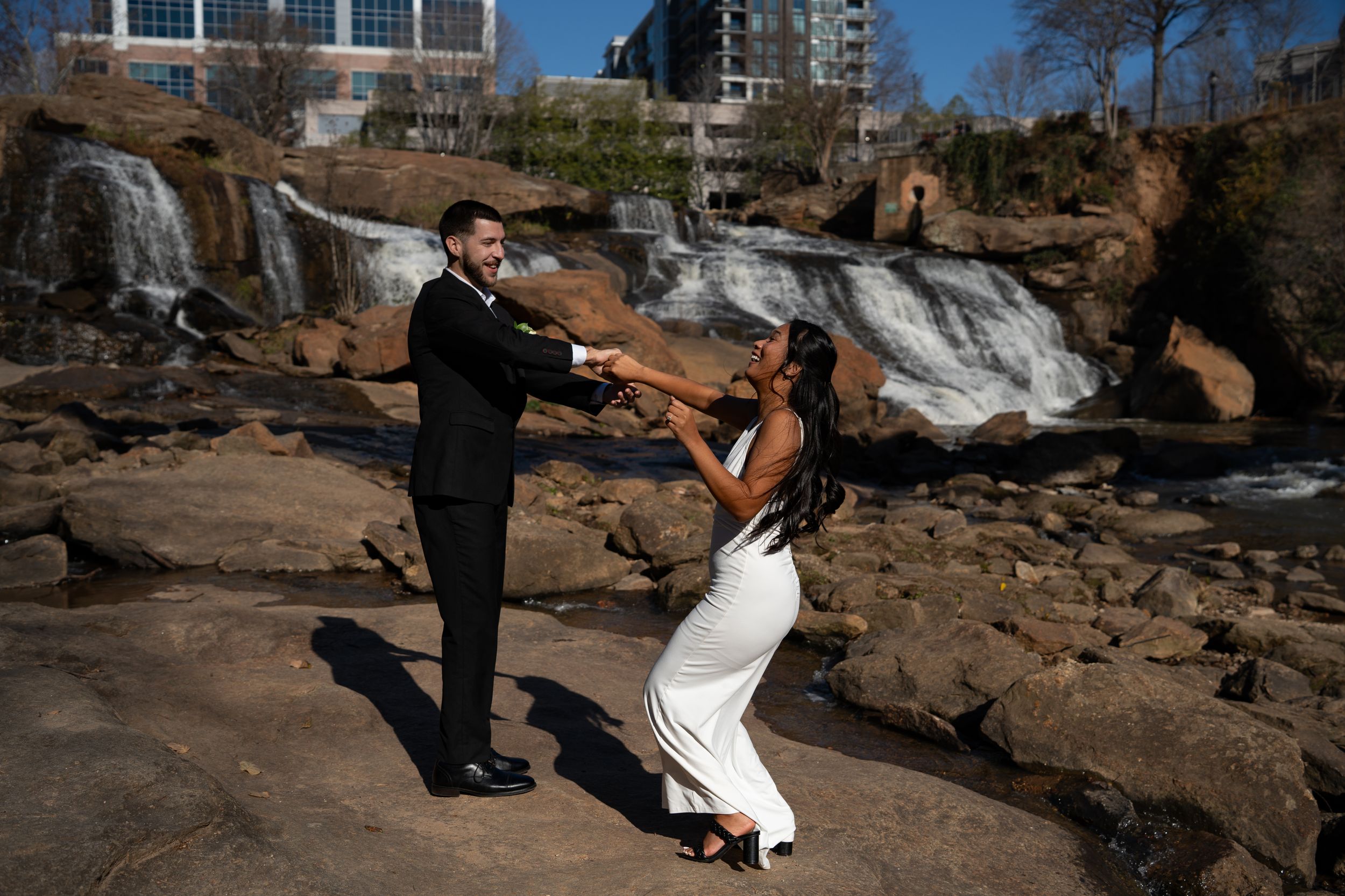 A couple poses together at a scenic waterfall location for engagement or wedding photos on a sunny day.