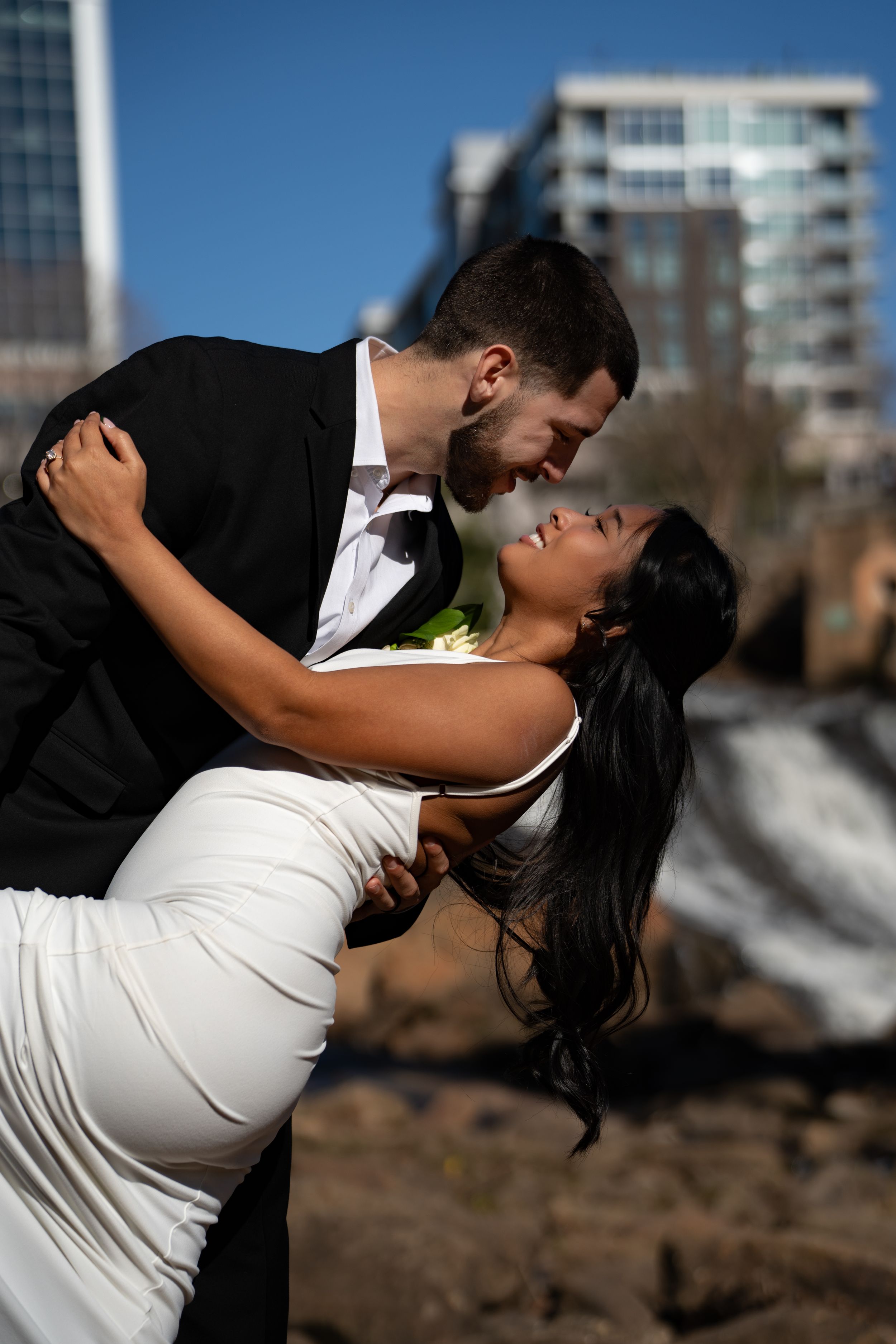 A romantic couple in formal attire dances and dips dramatically against an urban backdrop.