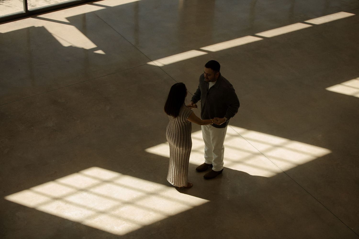 Engagement Shoot with dramatic shadows cast through windows on empty floor space.