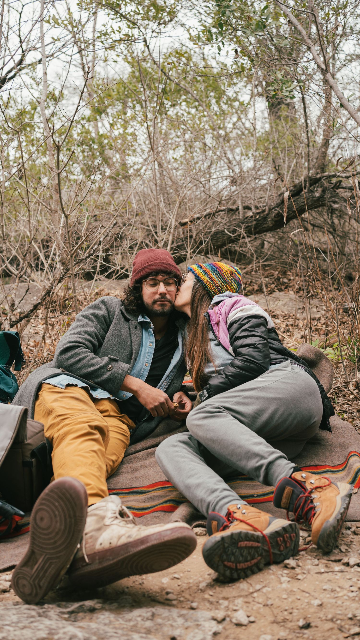 Two hikers resting on ground with backpacks in wooded area.