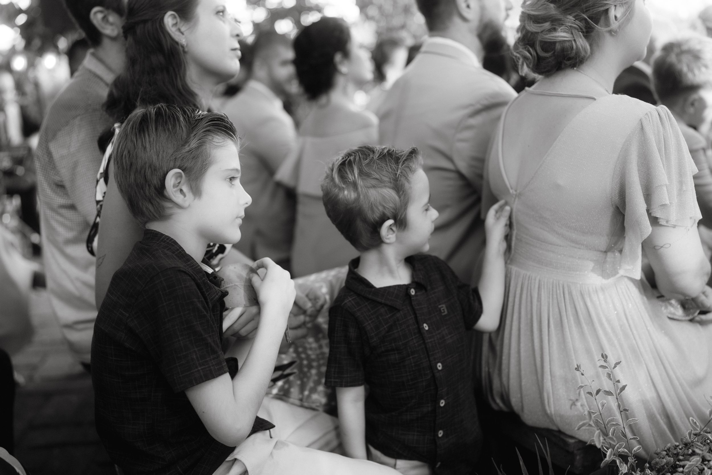 Black and white candid photo of young guests enjoying outdoor wedding celebration.