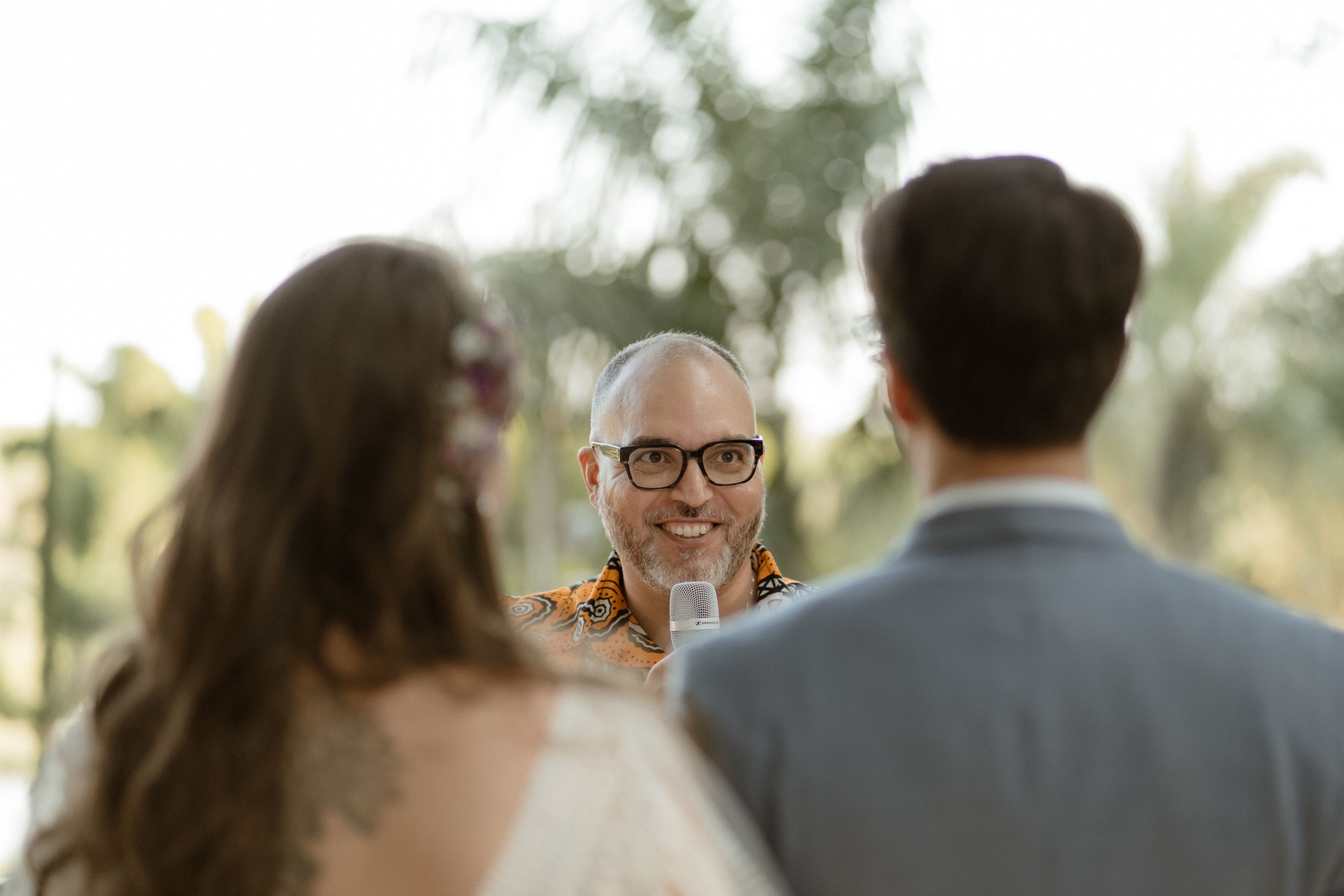 Intimate moment during outdoor wedding ceremony with natural sunlight filtering through trees.