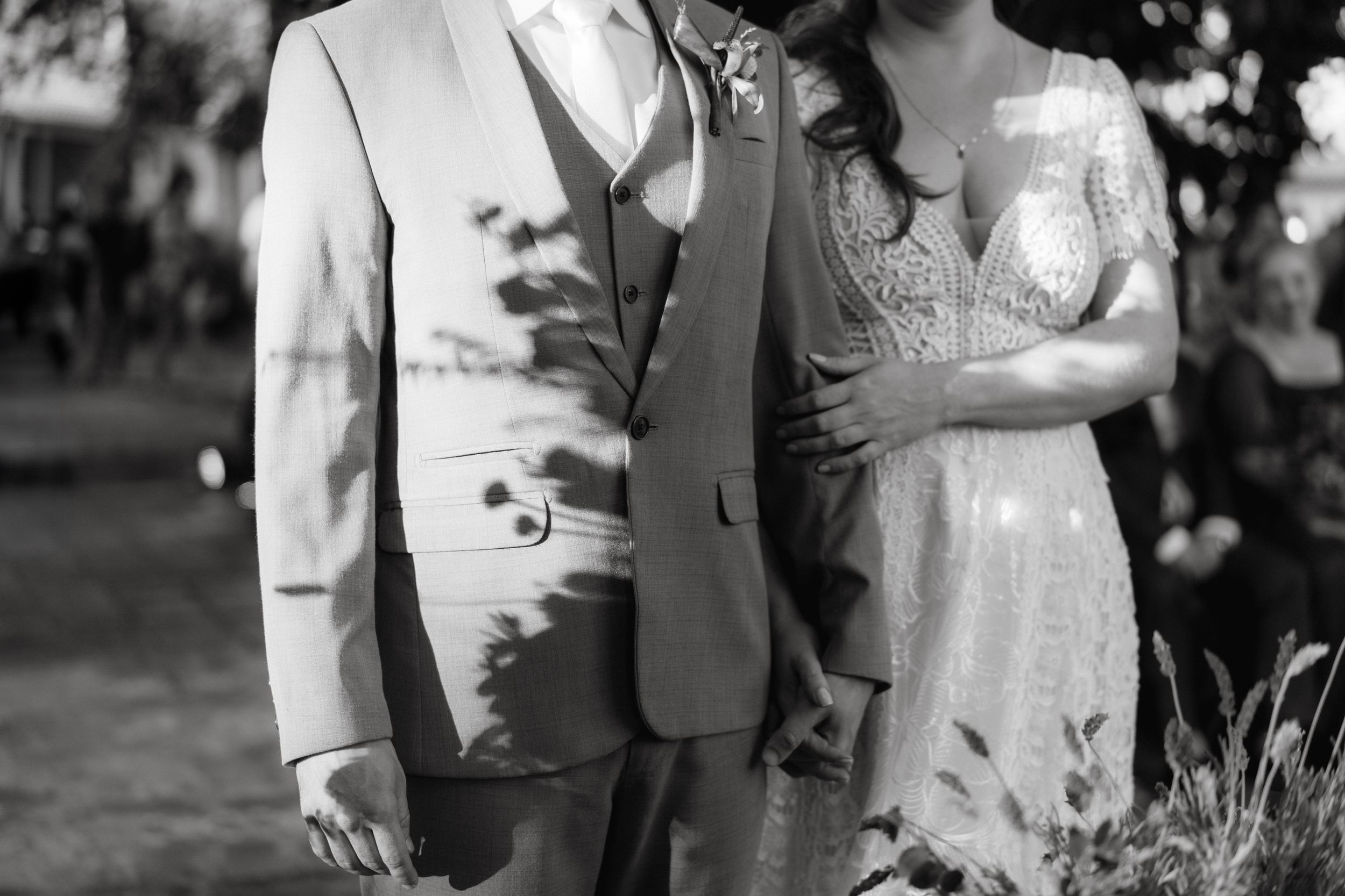 A couple in formal attire stands together in natural lighting during an outdoor event.