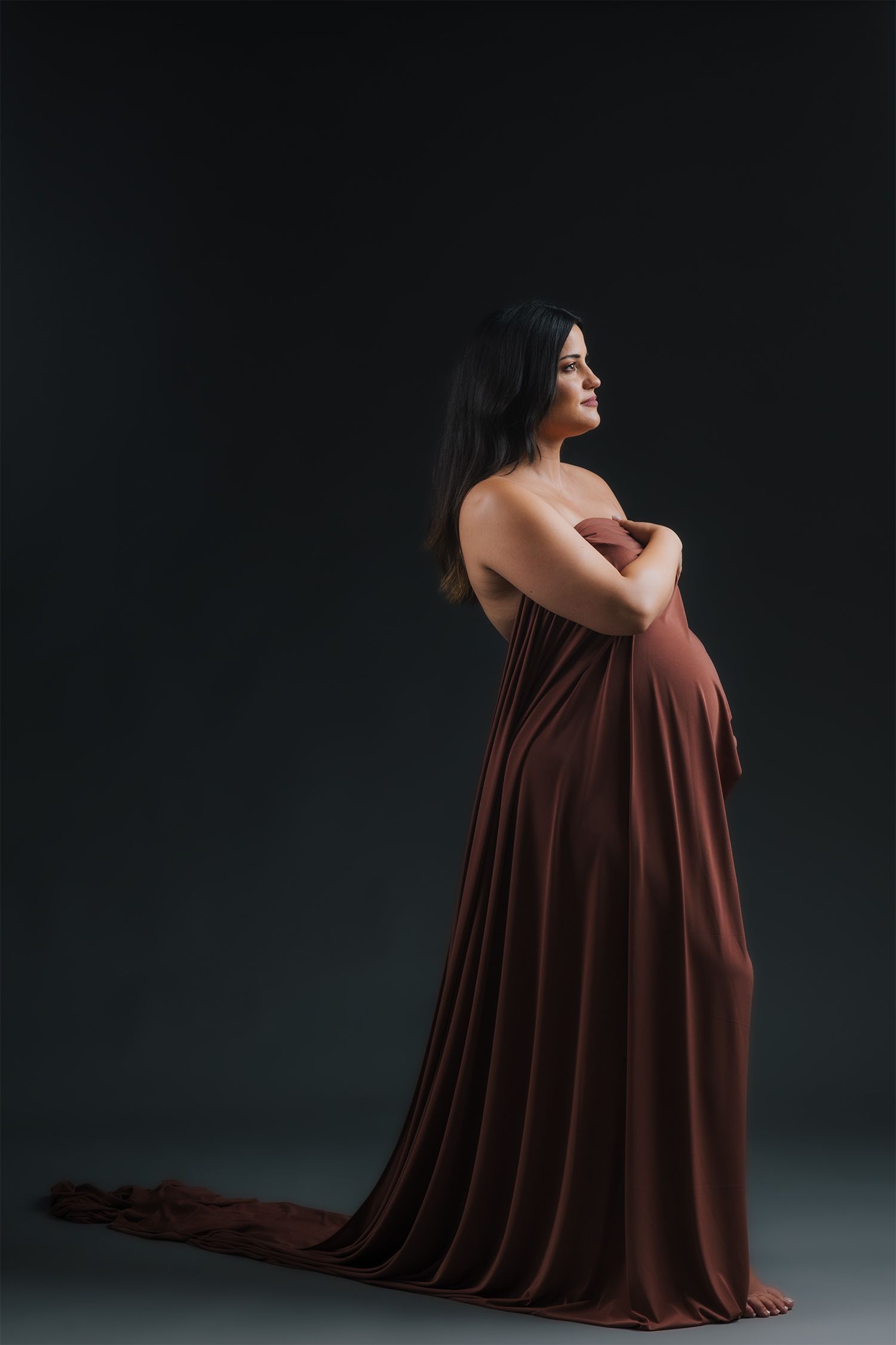 Intimate maternity portrait of couple embracing in dark studio setting.