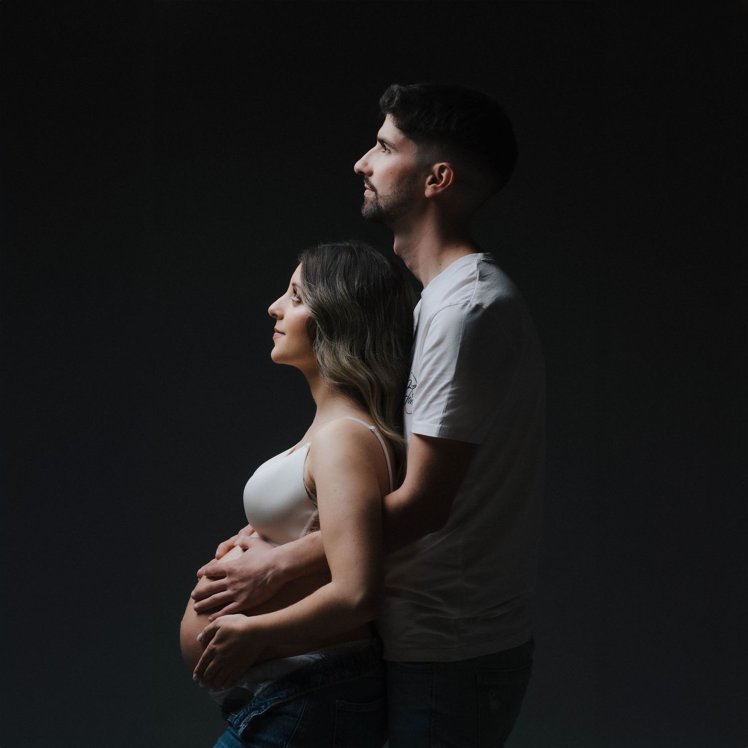 Intimate maternity portrait of couple embracing in dark studio setting.