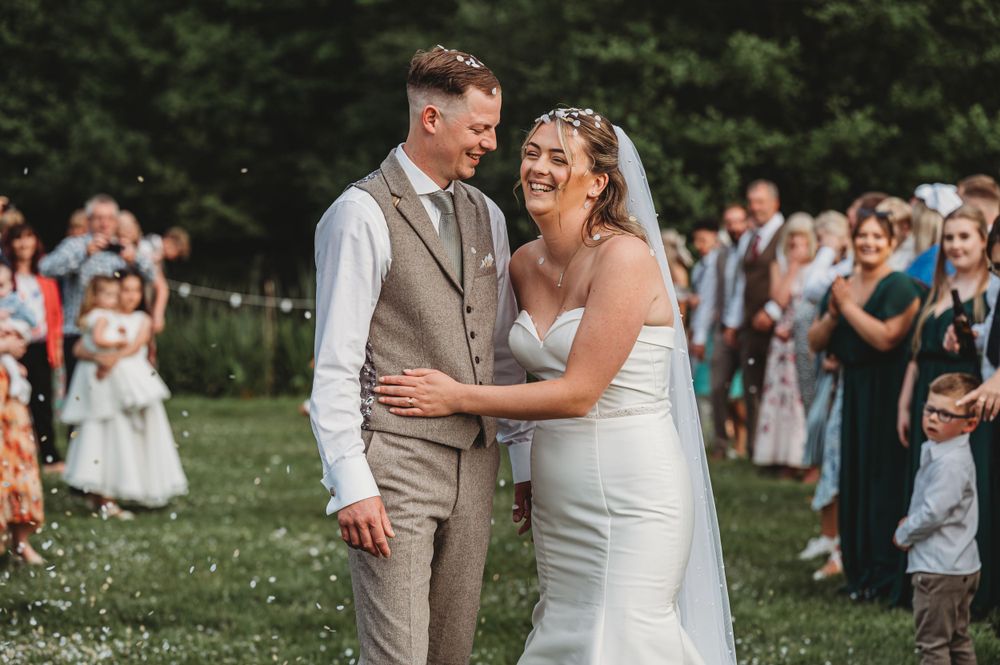 Happy newlyweds share a joyful moment while wedding guests look on in the background.