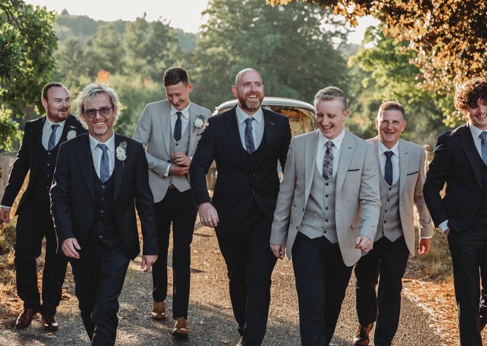 A wedding party of groomsmen walk together outdoors during sunset.