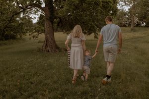 A family walks together through a grassy field on a summer evening.