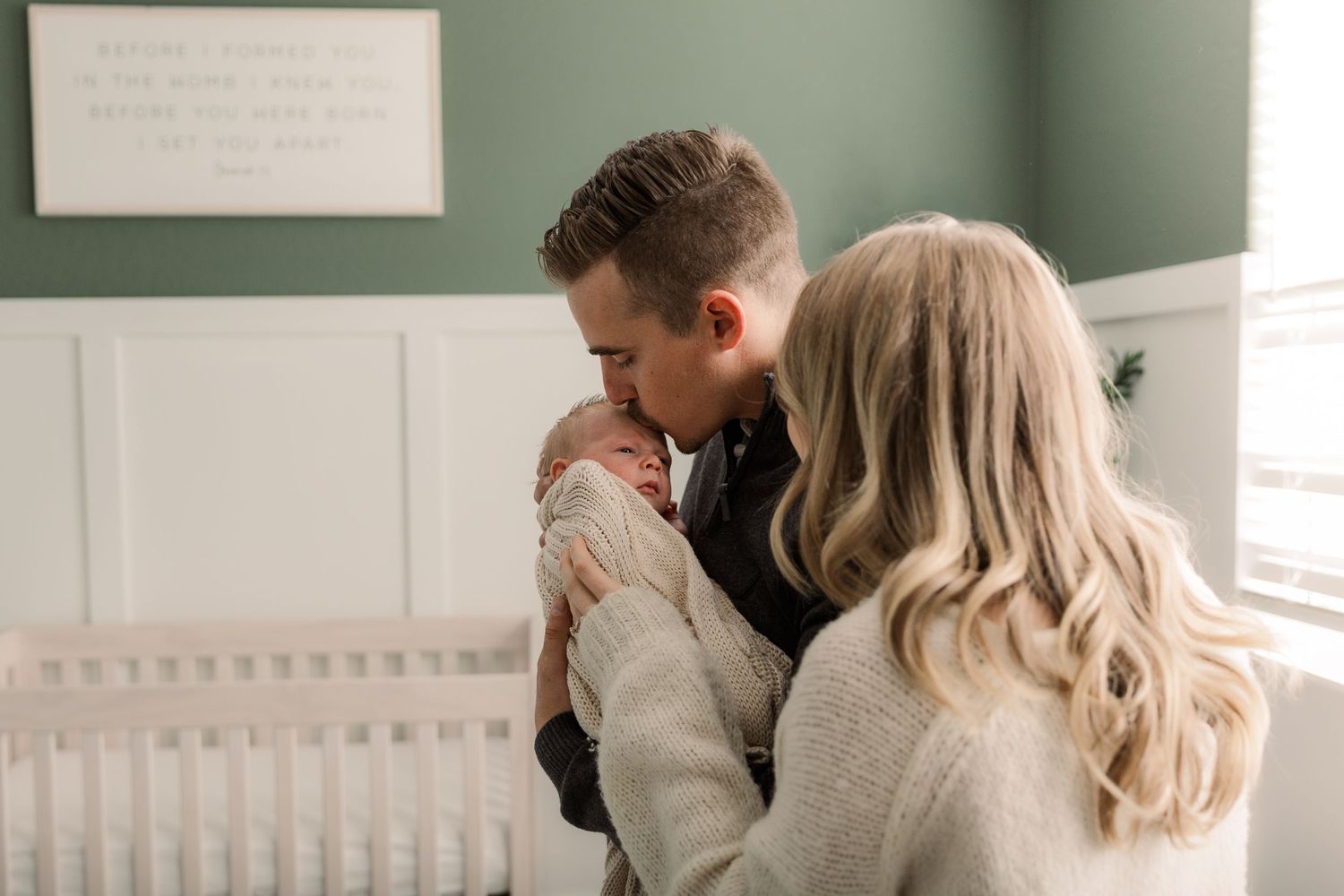 An intimate nursery scene with soft green walls and white wainscoting.