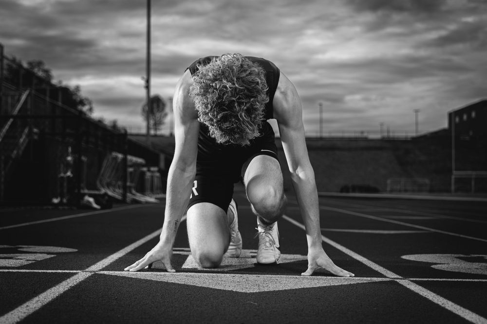 Black and white photo of a curly-haired athlete in starting position on a running track.