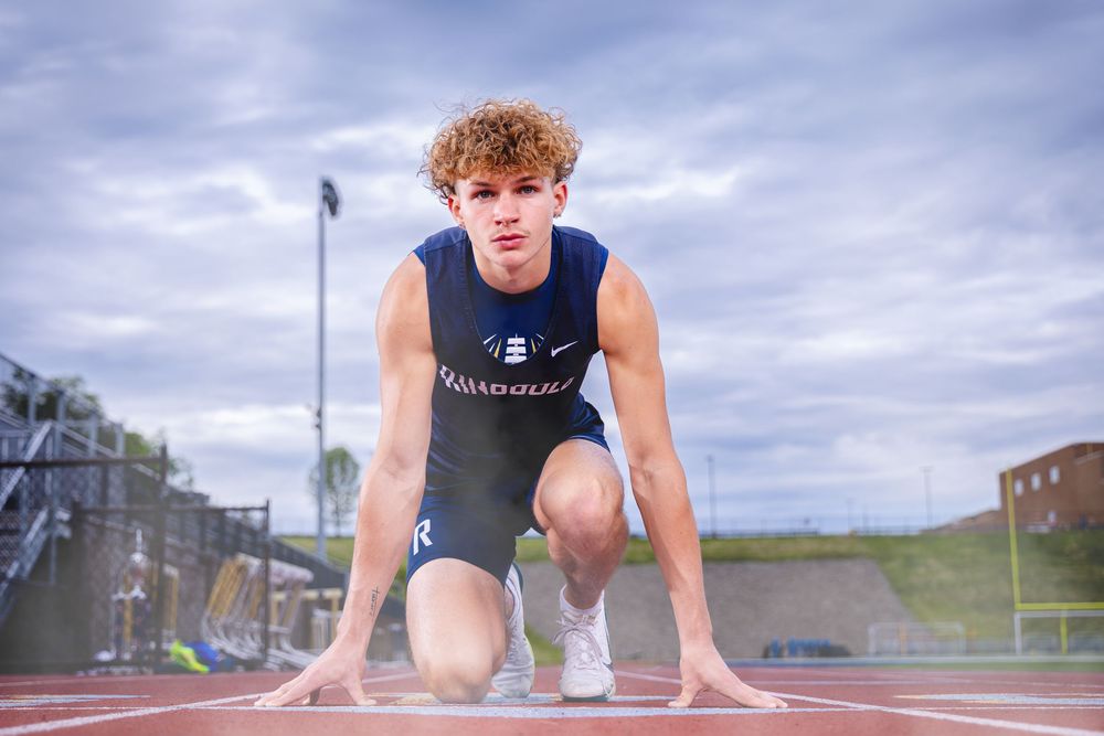 Young male sprinter in starting position on red track, wearing navy athletic uniform, ready to race.