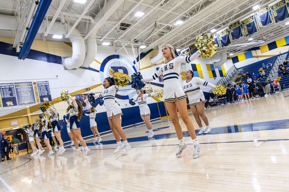 High school cheerleaders perform energetically in a blue and gold gymnasium during a pep rally.