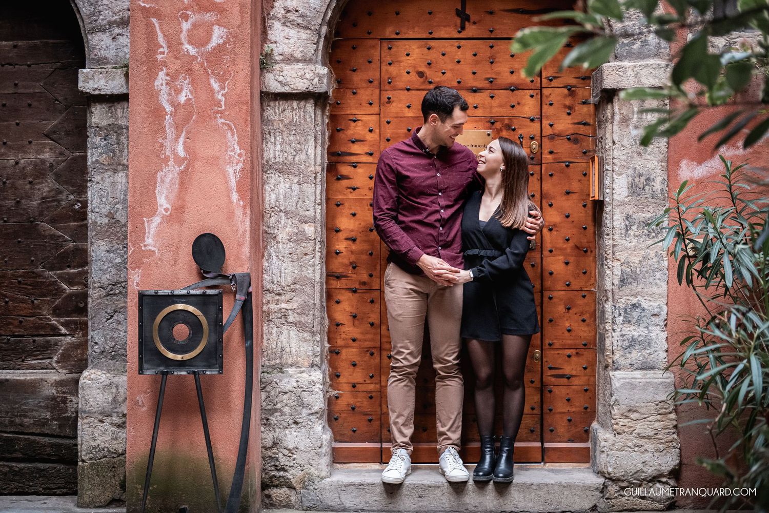 Couple poses against rustic brick and stone wall with vintage architectural details.