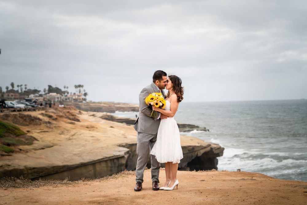 Couple sharing an intimate moment on coastal cliffs with yellow bouquet, wedding photographer.