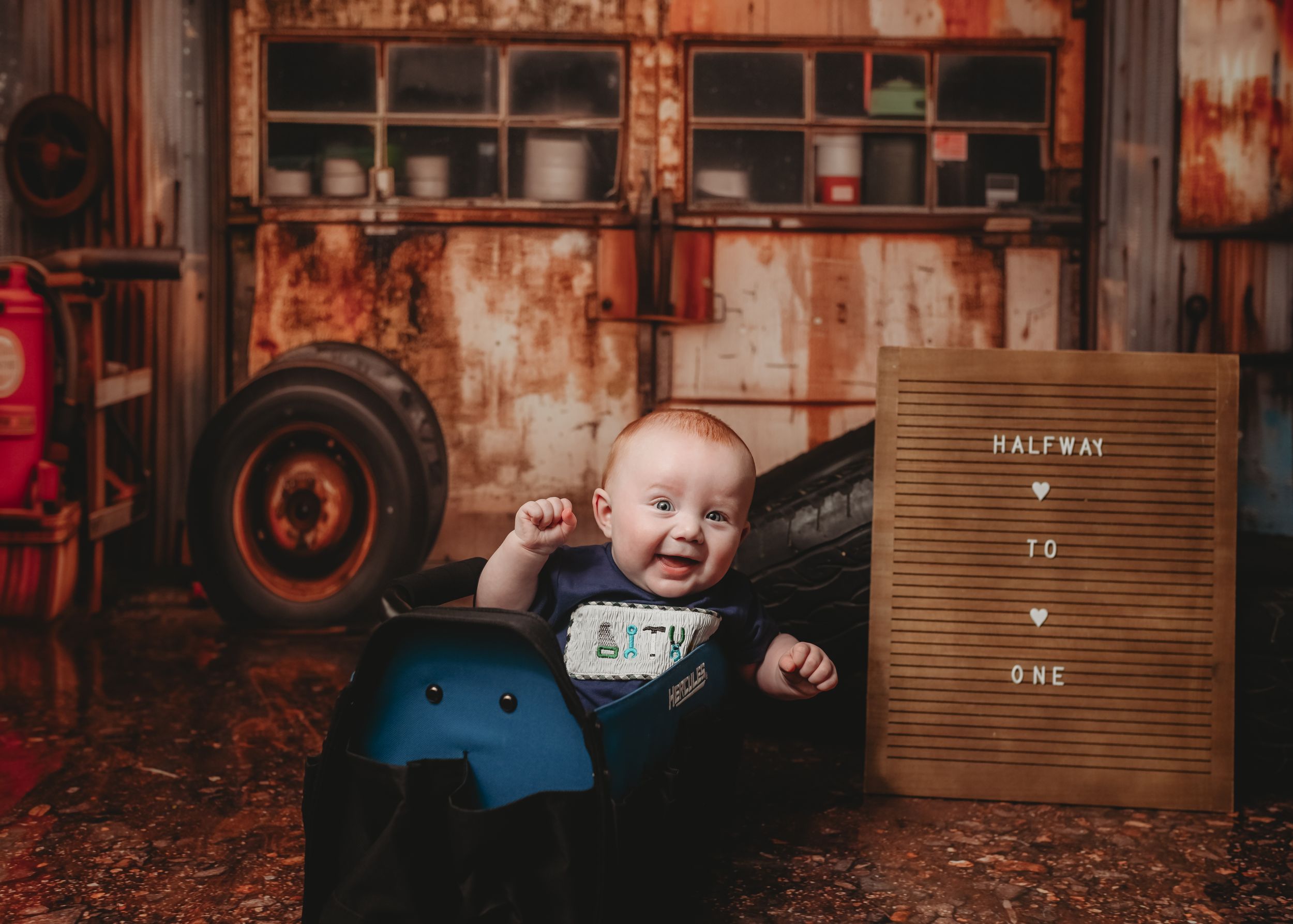 Baby sitting in blue container against rustic industrial backdrop with letterboard.