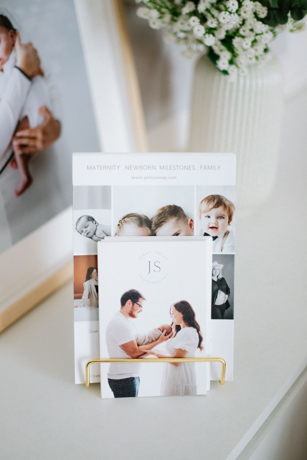 Business cards and photography prints displayed in a gold stand with white flowers in background.
