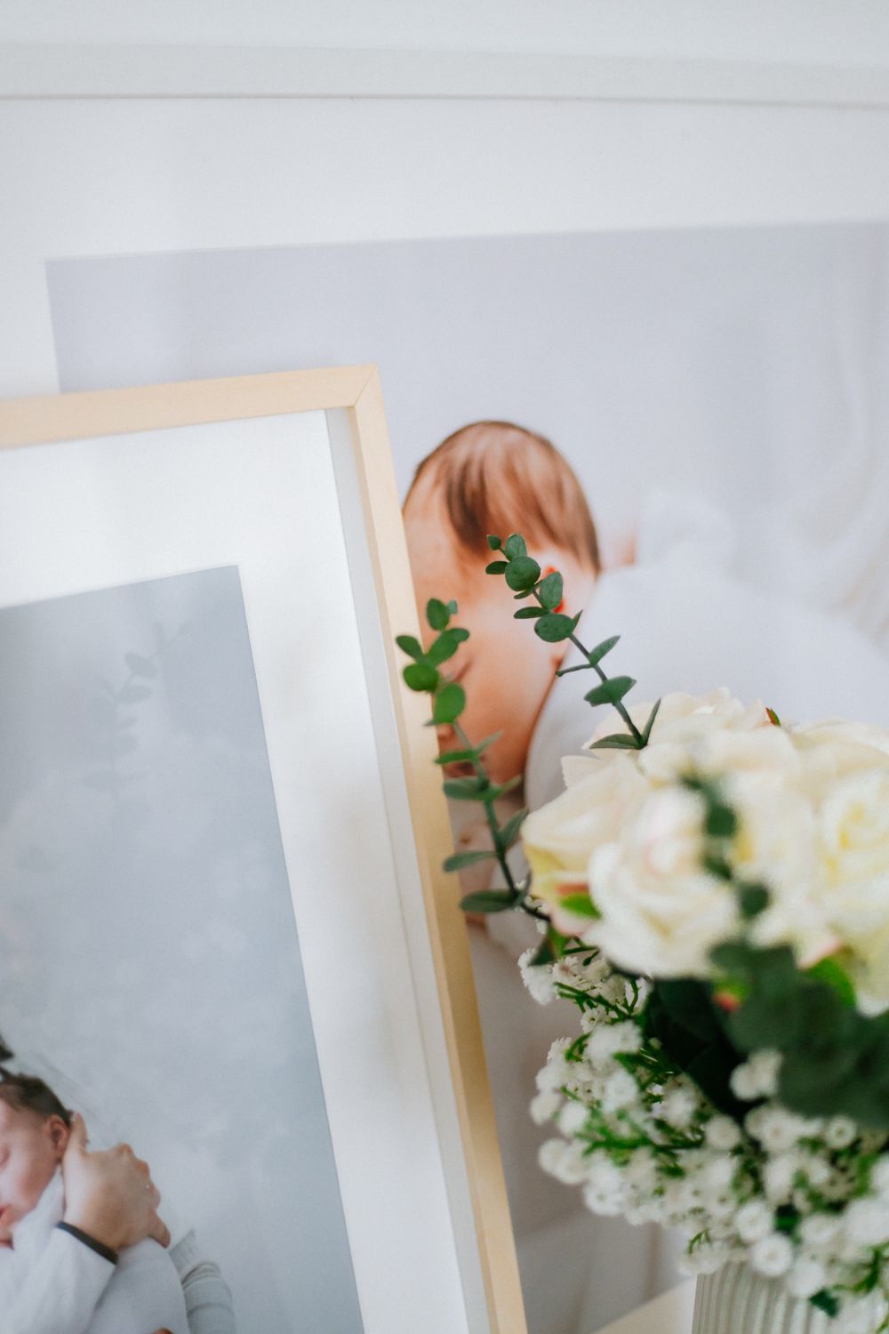 Picture frames and delicate white flowers with green foliage create an elegant still life composition.