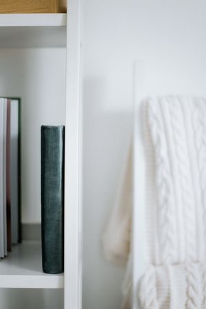 White knitted blanket hanging next to wooden shelf with dark hardcover books.