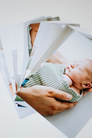 Hands holding a stack of photographs showing a baby wearing a mint green knit sweater.